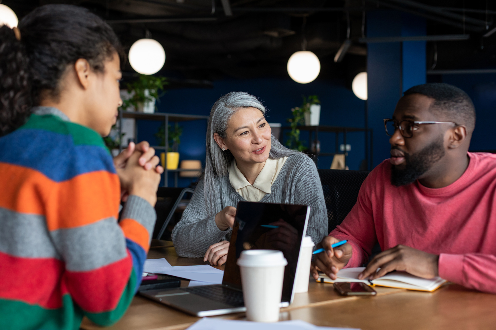 Two women and a man sitting around a table with a desktop on it