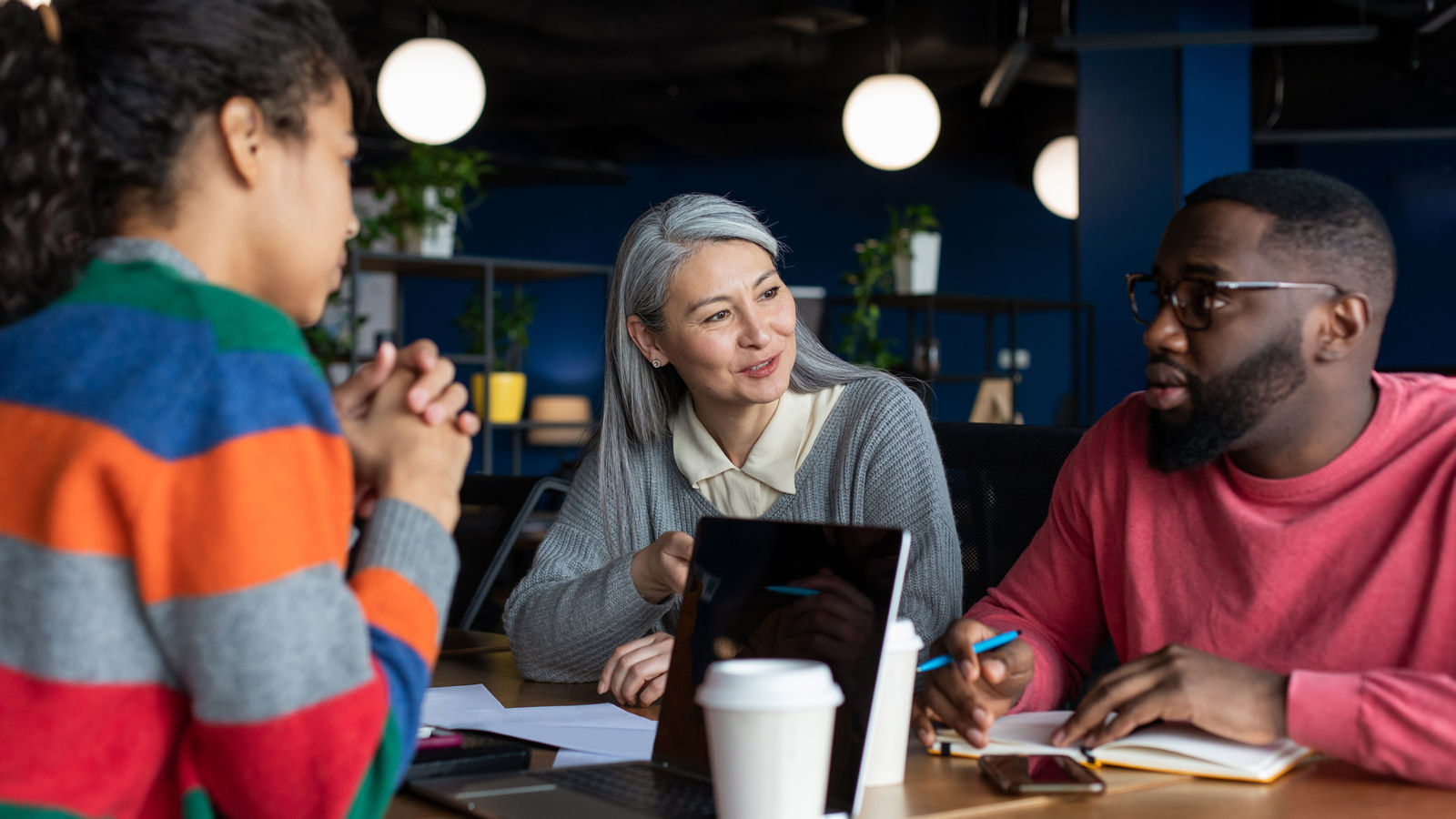 Two women and a man sitting around a table with a desktop on it